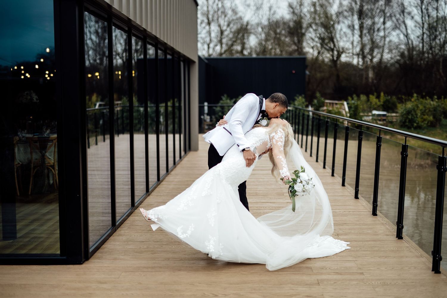 Groom dipping bride in a romantic outdoor pose, her white gown flowing on a modern deck.