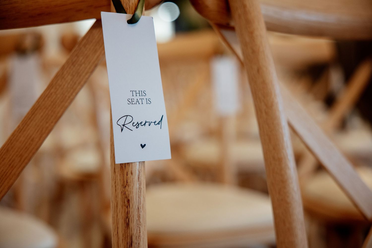 A reserved seat tag hanging on a wooden cross-back chair at a wedding venue.