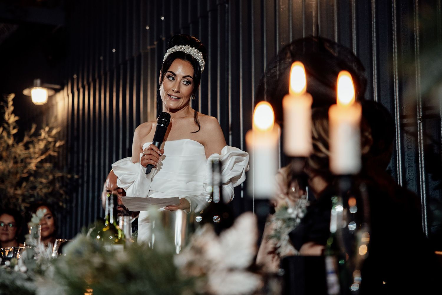 Candlelit wedding reception with dark industrial decor and hanging pendant lights creating an intimate atmosphere.