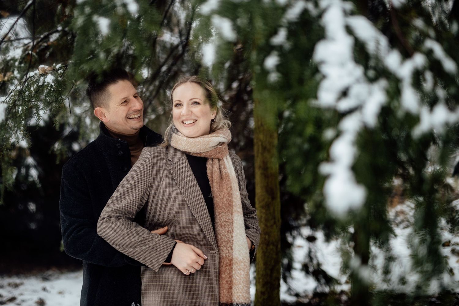 A romantic winter engagement photoshoot in a snowy forest setting with soft natural lighting.