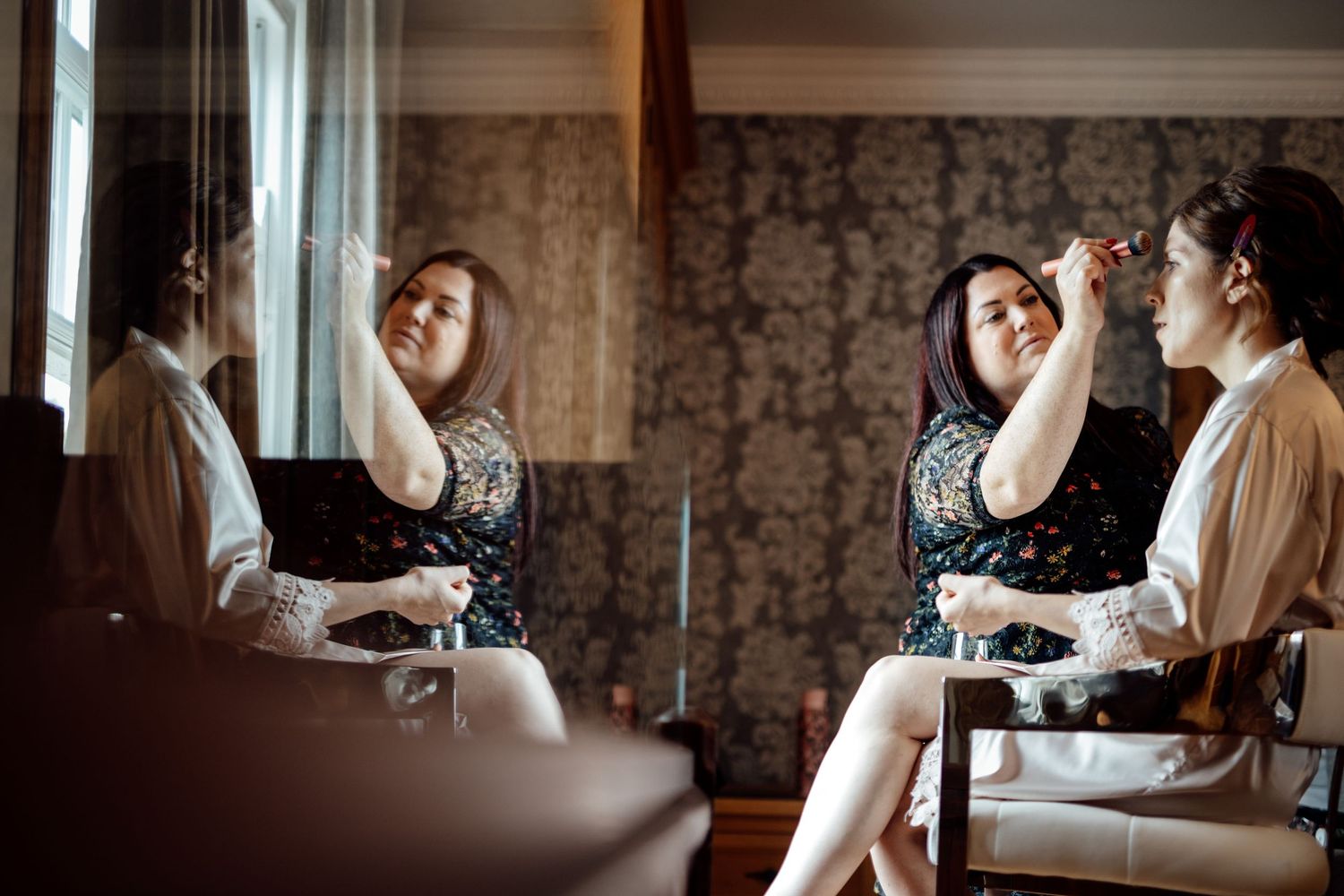 Wedding preparation moments captured in a room with vintage wallpaper and natural lighting.