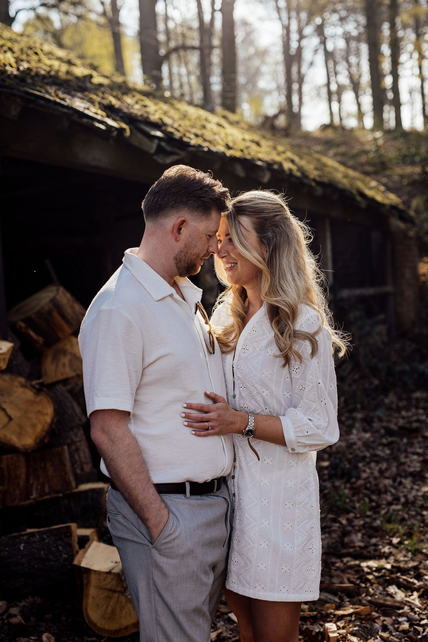 An intimate engagement photoshoot near stacked firewood in a forest setting.