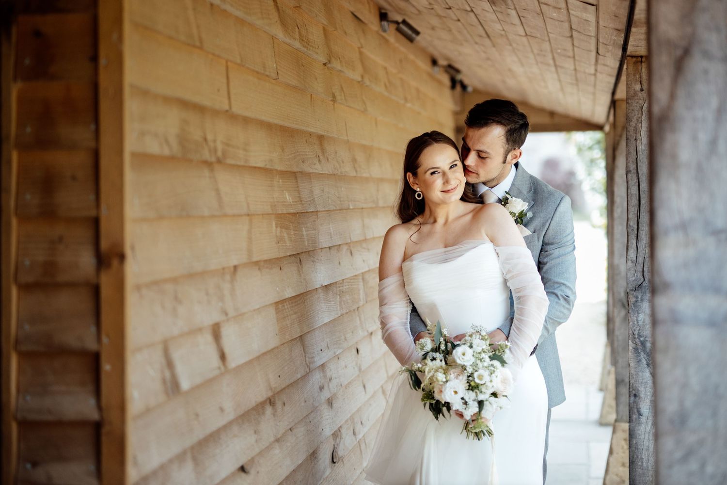 Elegant wedding couple poses against rustic wooden wall backdrop.