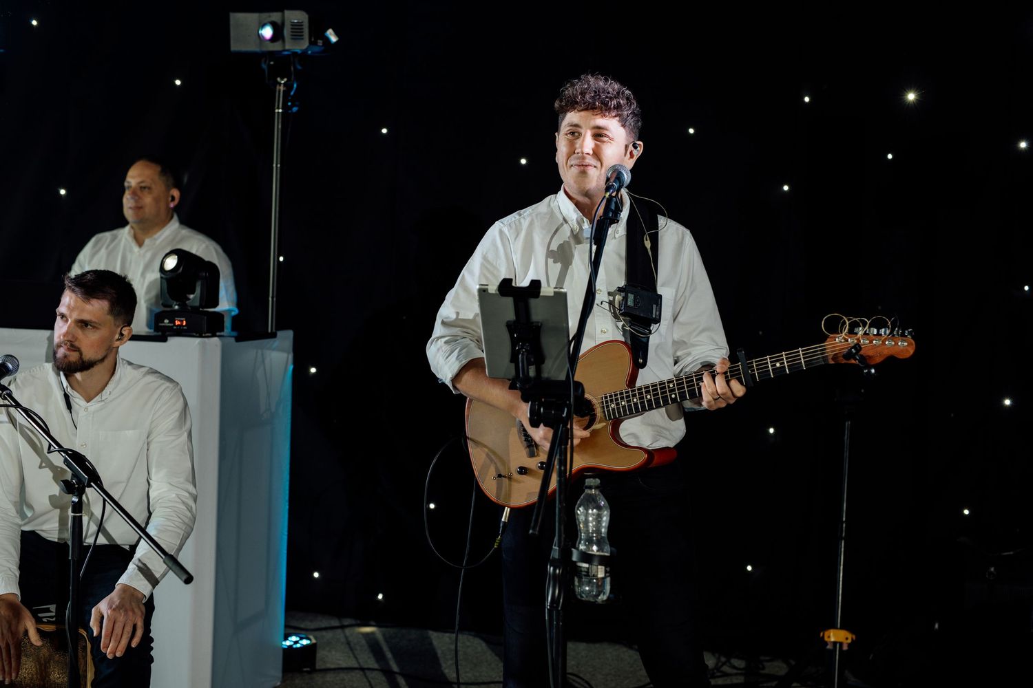 A musician performs on stage with a guitar during an evening event.