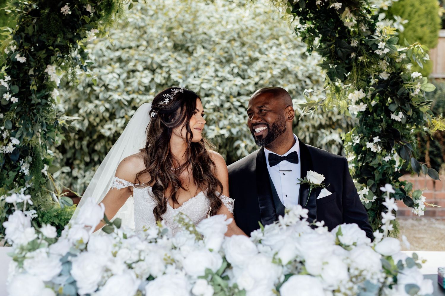 Elegant outdoor wedding portrait session with white floral arrangements in background.