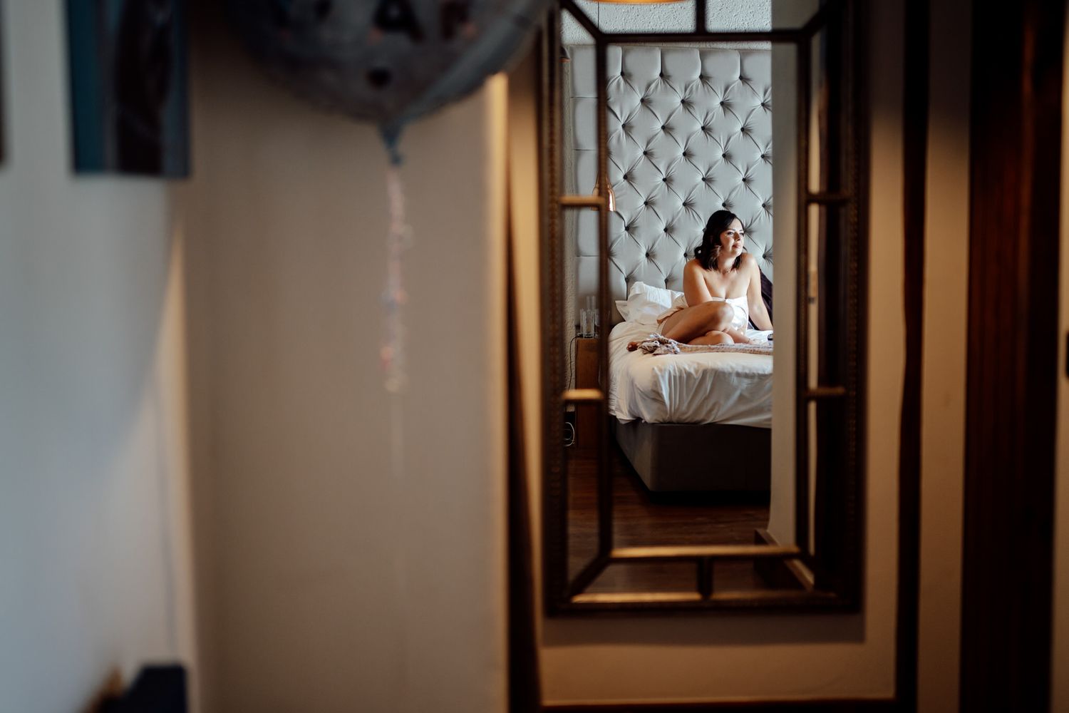 Sunlit hallway leading to a bedroom with vintage mirror and soft lighting.