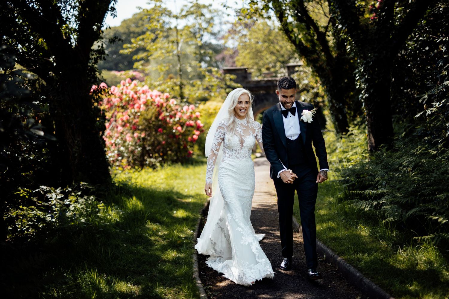 Couple walks through a garden path with blooming spring flowers and greenery.