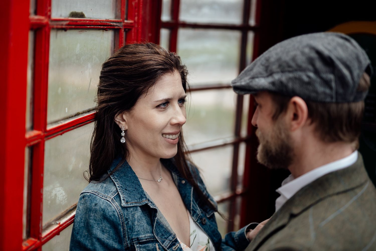 Couple shares intimate moment near red telephone booth in vintage setting.