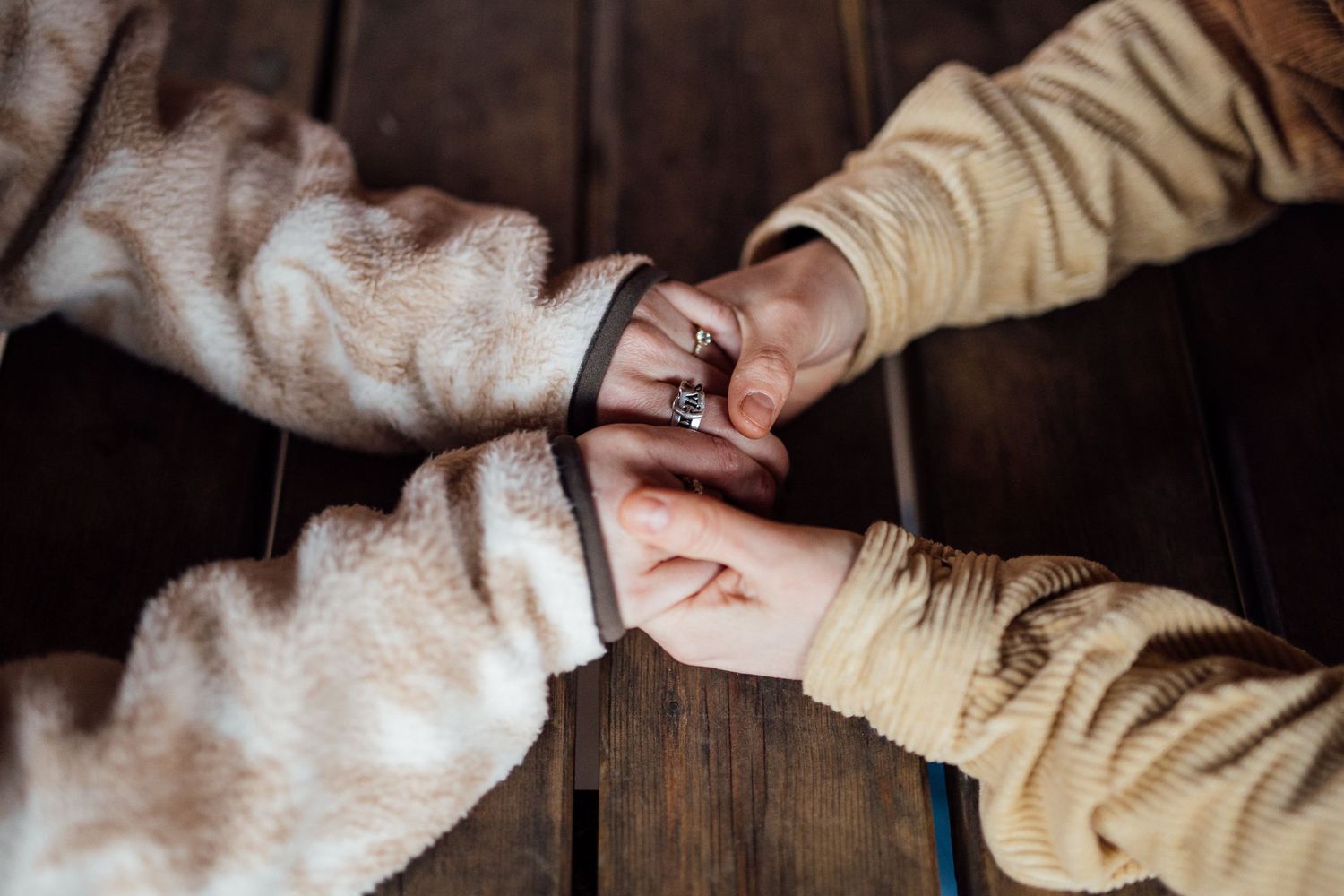 Close-up of couple's hands with engagement ring in focus during outdoor winter photoshoot.