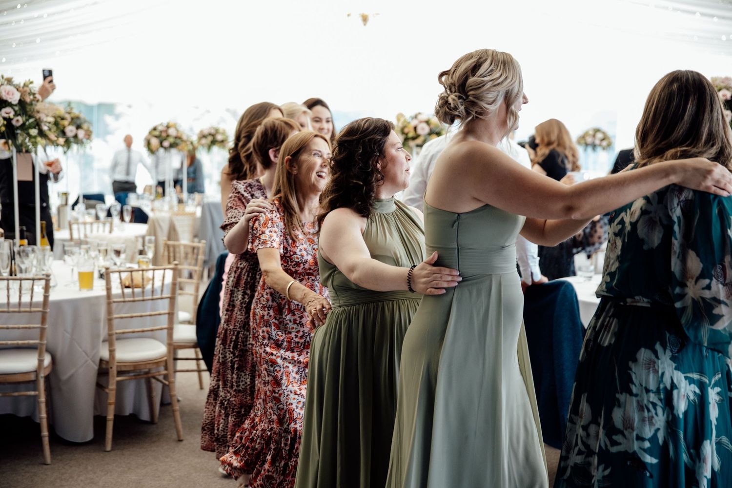 Wedding guests dancing in a bright reception hall with white decor.