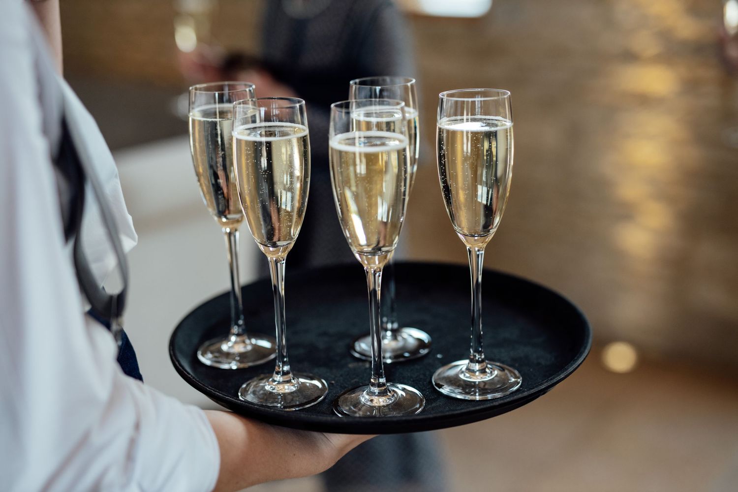 Champagne flutes on a black serving tray being carried by a server at a wedding reception.