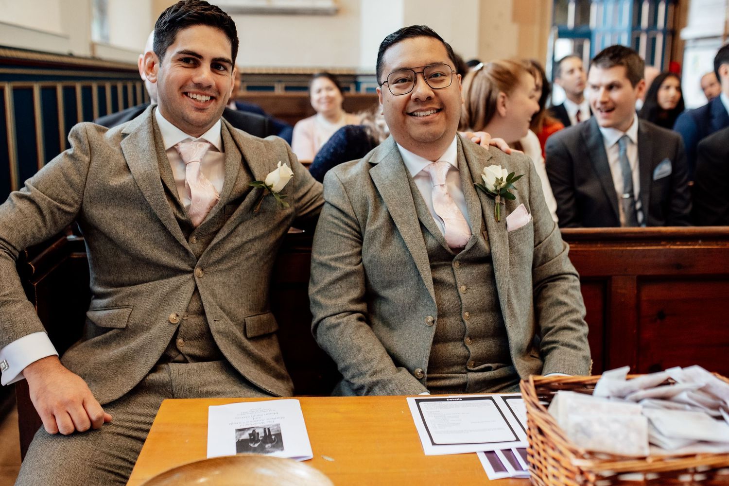Wedding party seated in church pews wearing coordinated gray suits.