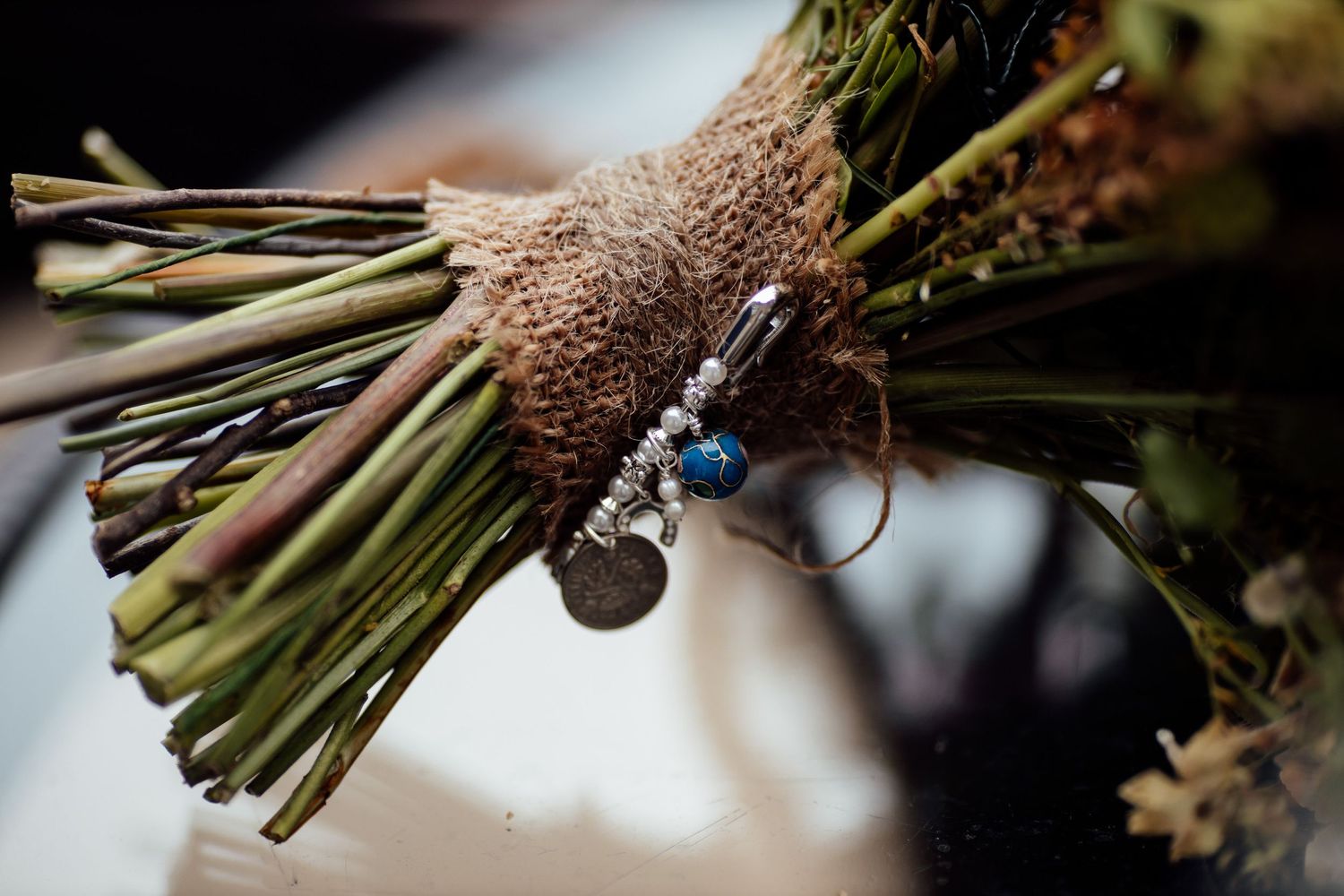 Close-up detail of a rustic wedding bouquet wrapped with twine and decorated with charms.