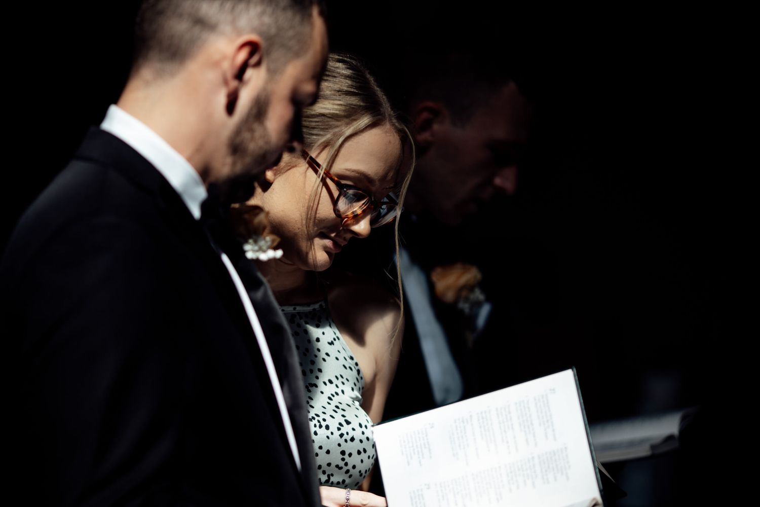 Two people in formal attire sharing an intimate moment in low light.