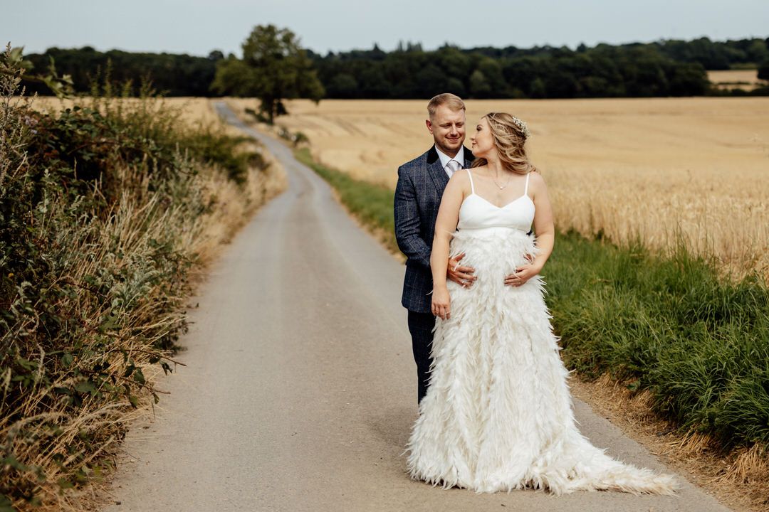 A wedding couple poses on a scenic rural path with wheat fields stretching into the distance.