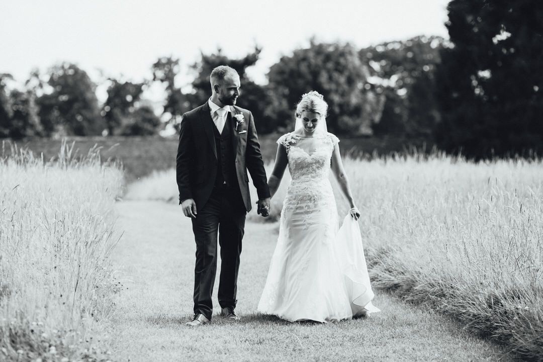 Black and white photo of wedding party walking through a grassy field.