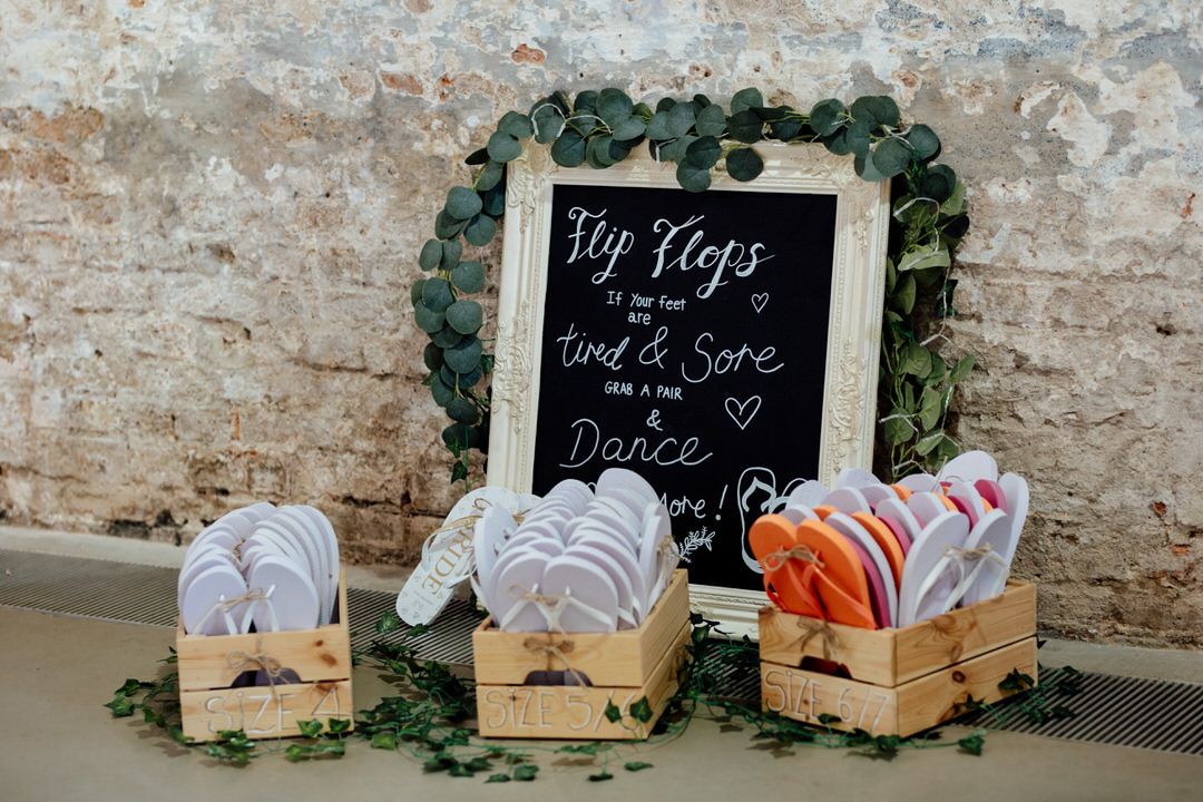 Wedding reception details featuring rustic wooden boxes with chalkboard signs and greenery decorations.