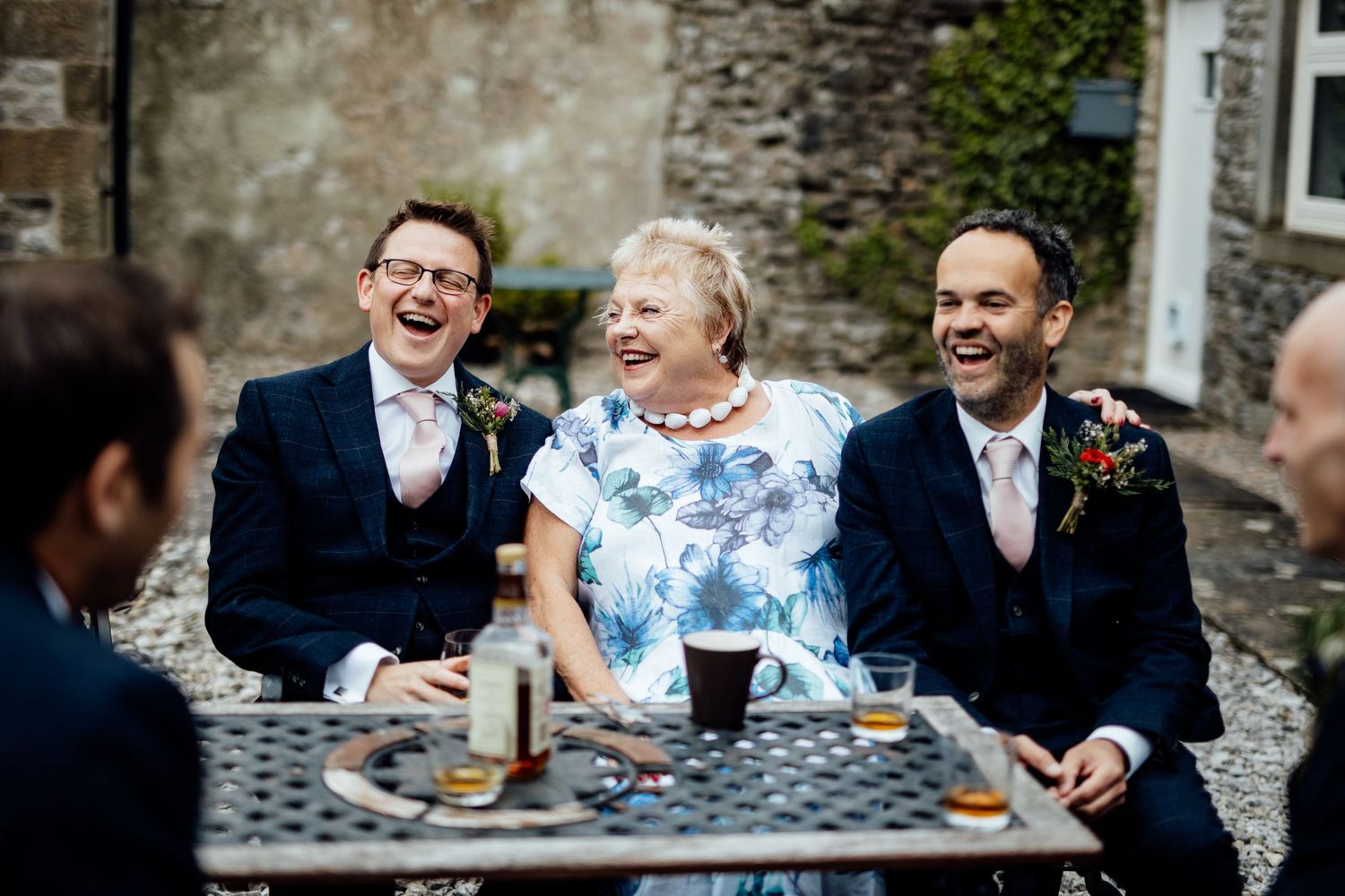 Wedding guests sharing laughter and drinks at outdoor tables.