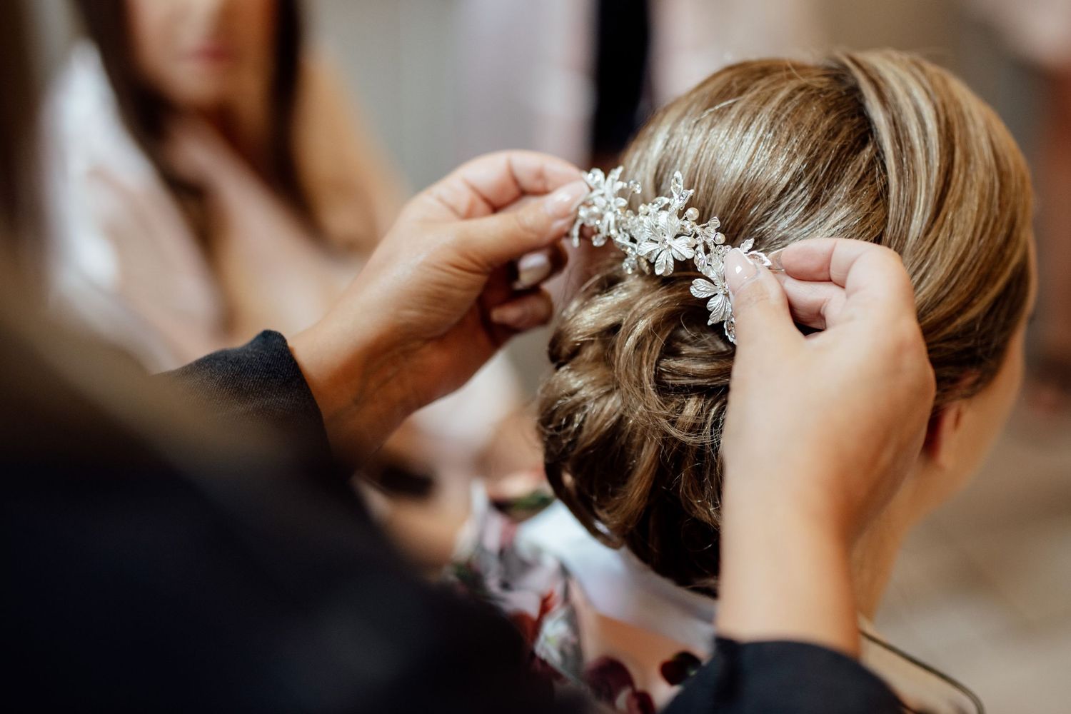 Close-up of hands placing an ornate hair accessory into an elegant bridal updo.