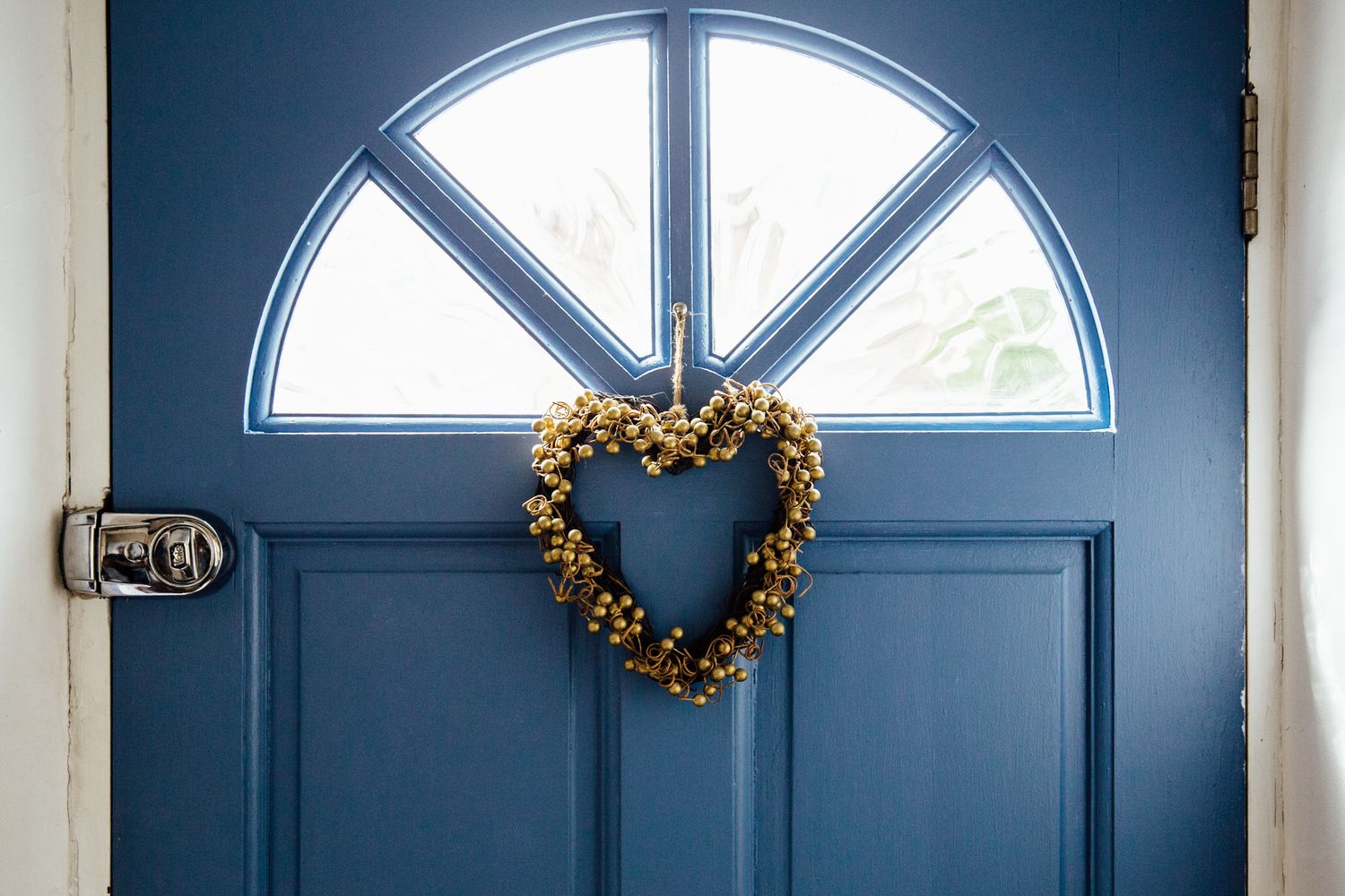 Navy blue front door with arched windows and decorative wreath in bright daylight.