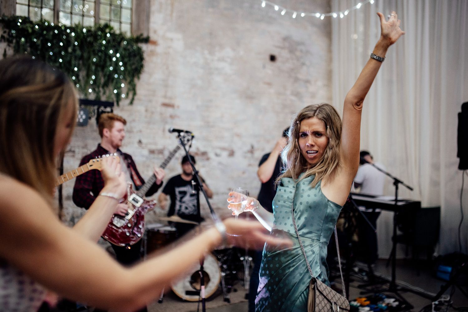 Wedding celebration with string lights and guests dancing in an industrial venue.