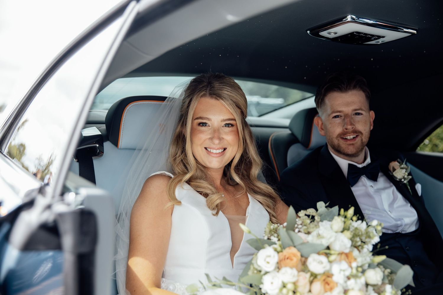 Newlyweds sharing a moment in their wedding car with bouquet.