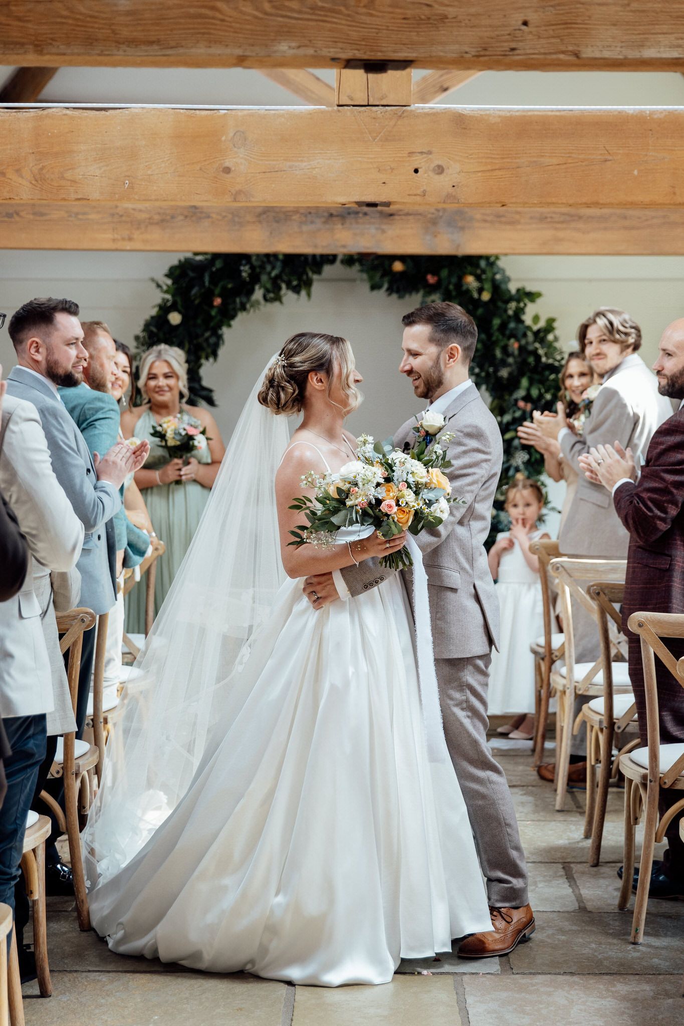 Wedding party members dance and celebrate in an elegant indoor venue with wooden beams.
