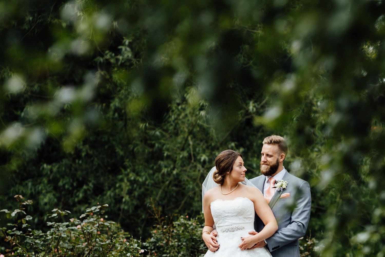 Newlyweds share an intimate moment surrounded by leafy green foliage.