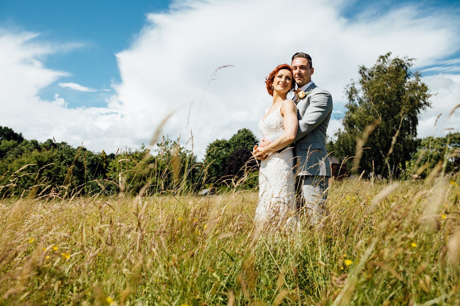 A romantic outdoor wedding portrait taken in a sunlit meadow with tall grass.