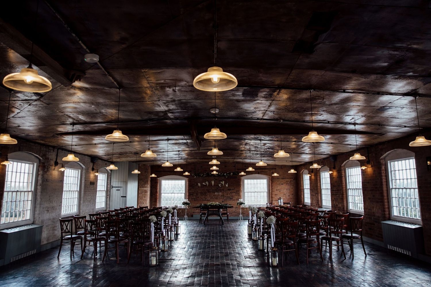 Empty reception hall with wooden floors and industrial ceiling lights creating dramatic perspective.