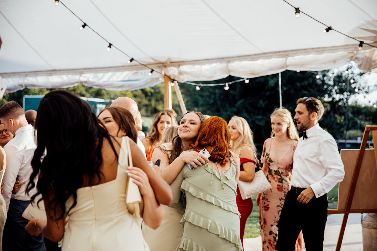 Wedding guests dancing and celebrating under string lights at outdoor reception.
