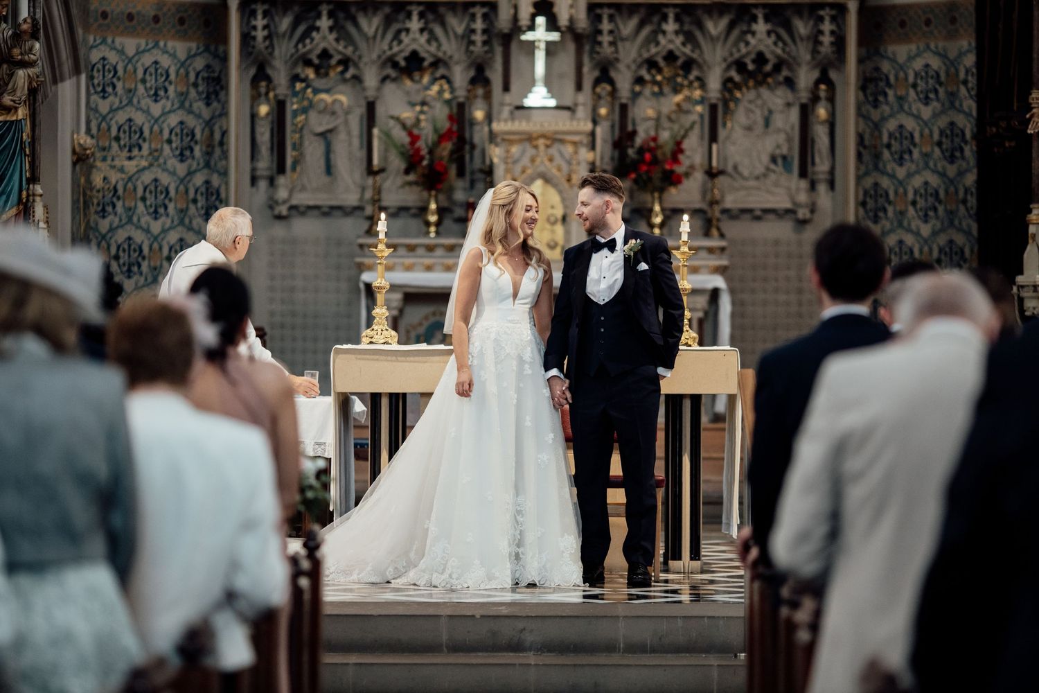 Wedding ceremony in an ornate church with gothic architectural details and candles on the altar.