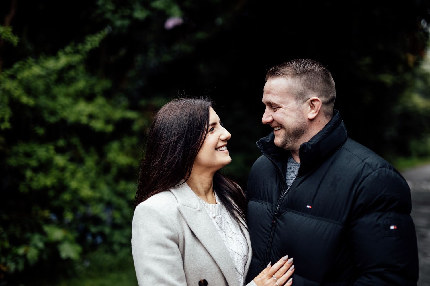 A couple shares joyful laughter while standing together in a wooded setting.