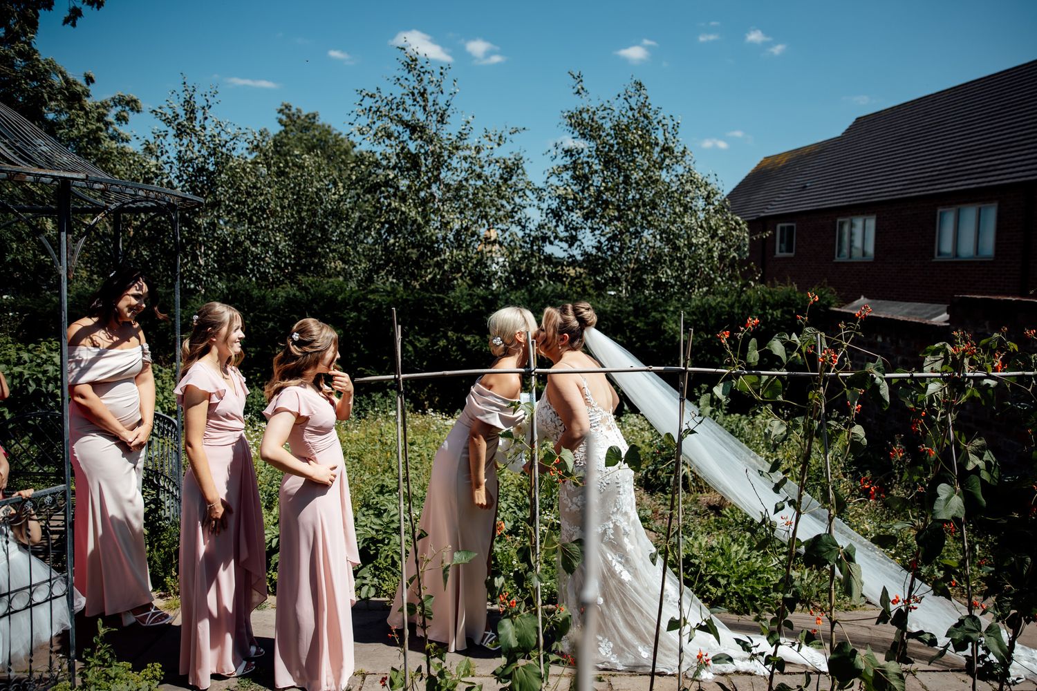 Wedding party poses outdoors against lush garden backdrop on sunny day.