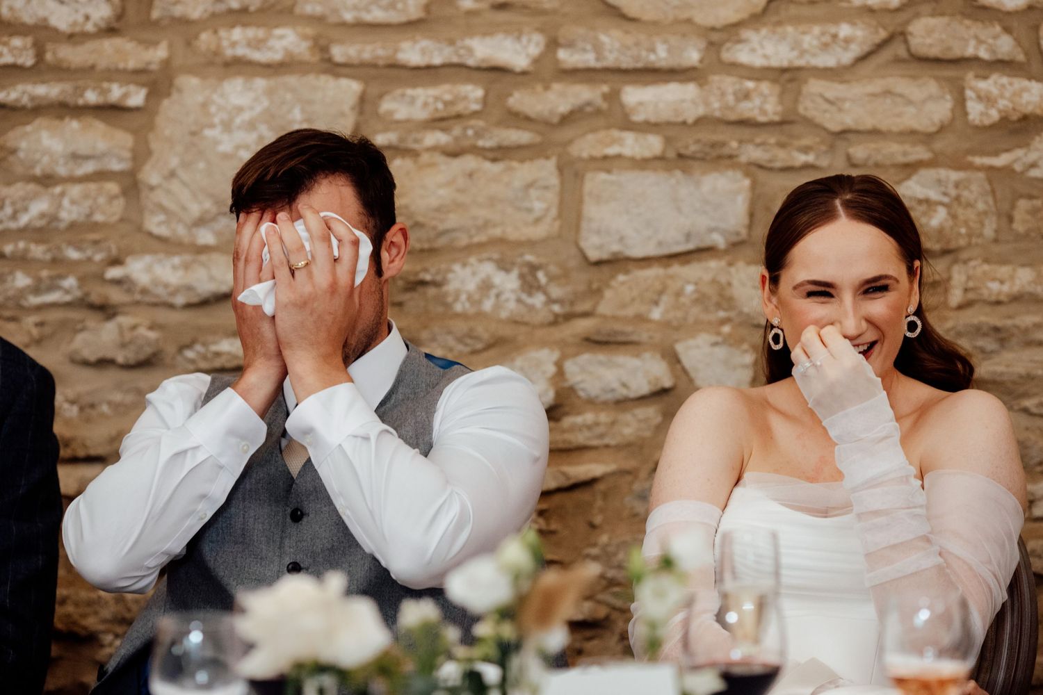 Wedding couple sharing emotional moment during reception speeches at stone-walled venue.
