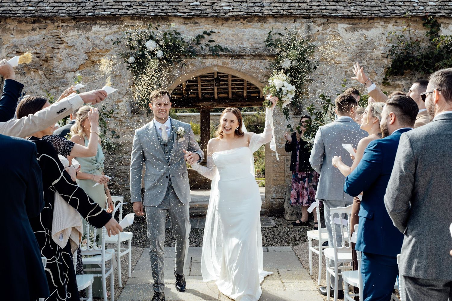 Wedding ceremony in progress inside rustic stone barn with white chairs.