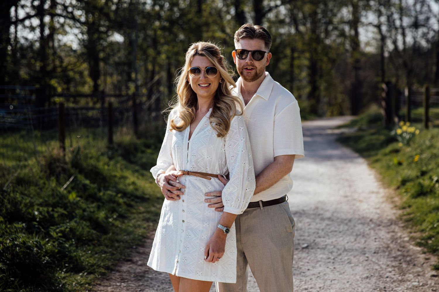 Two people share an intimate moment while walking on a sunlit nature trail.