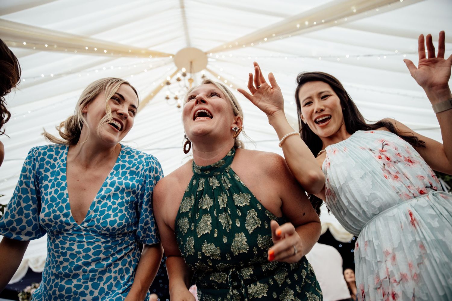 Wedding guests dancing and celebrating joyfully at a reception under a white tent.