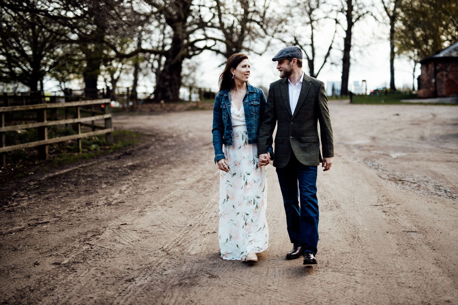 A couple takes a romantic stroll along a tree-lined path in casual attire.