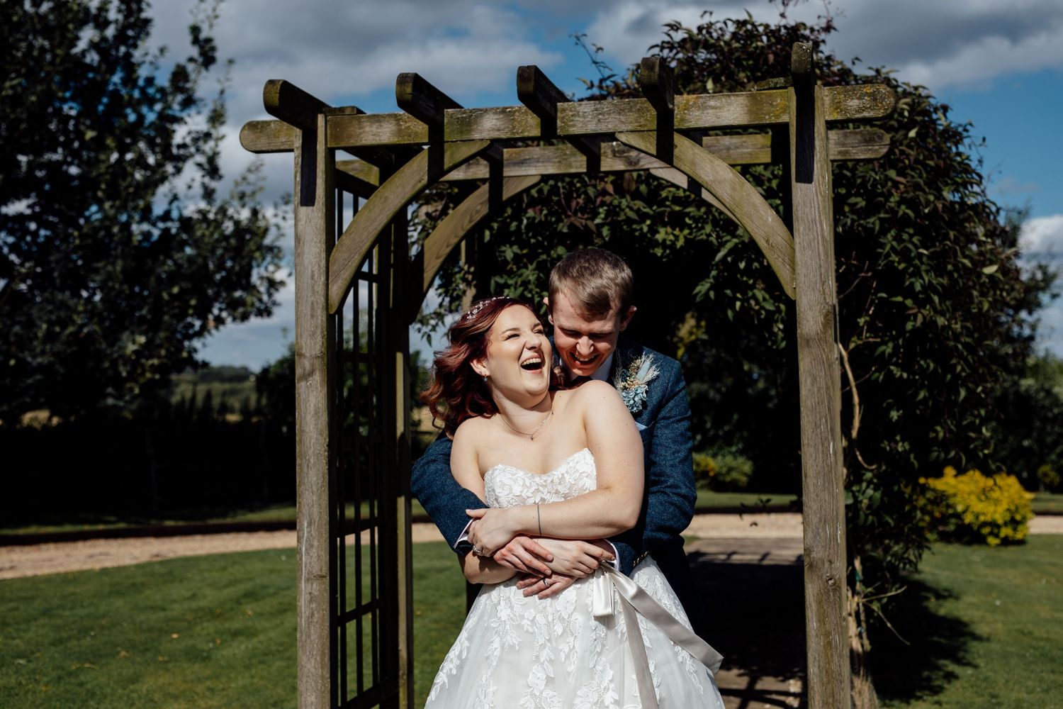 Newlyweds share romantic moments under a wooden pergola in a garden setting.