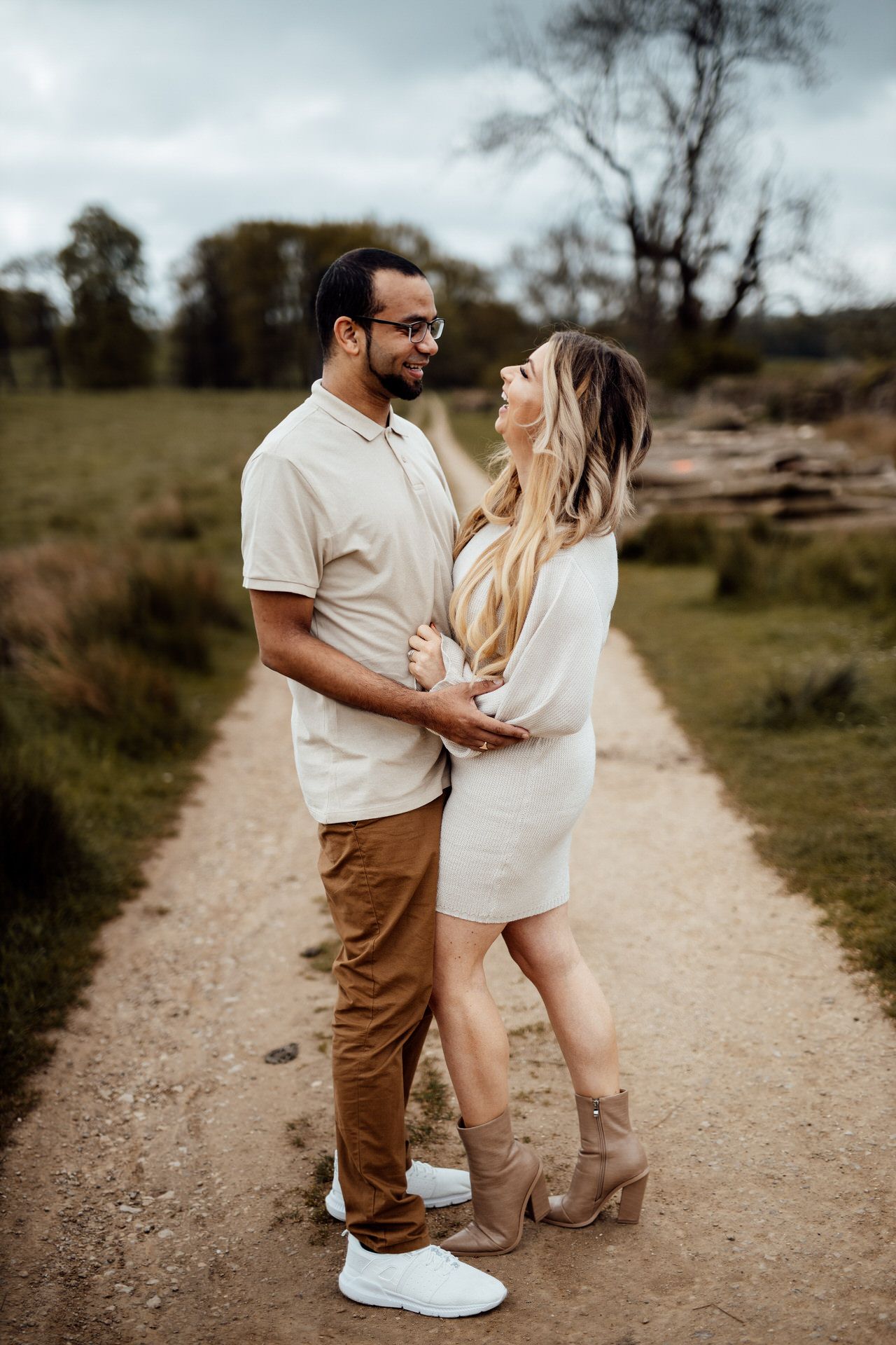 A romantic couple shares tender moments on a dirt path surrounded by nature.