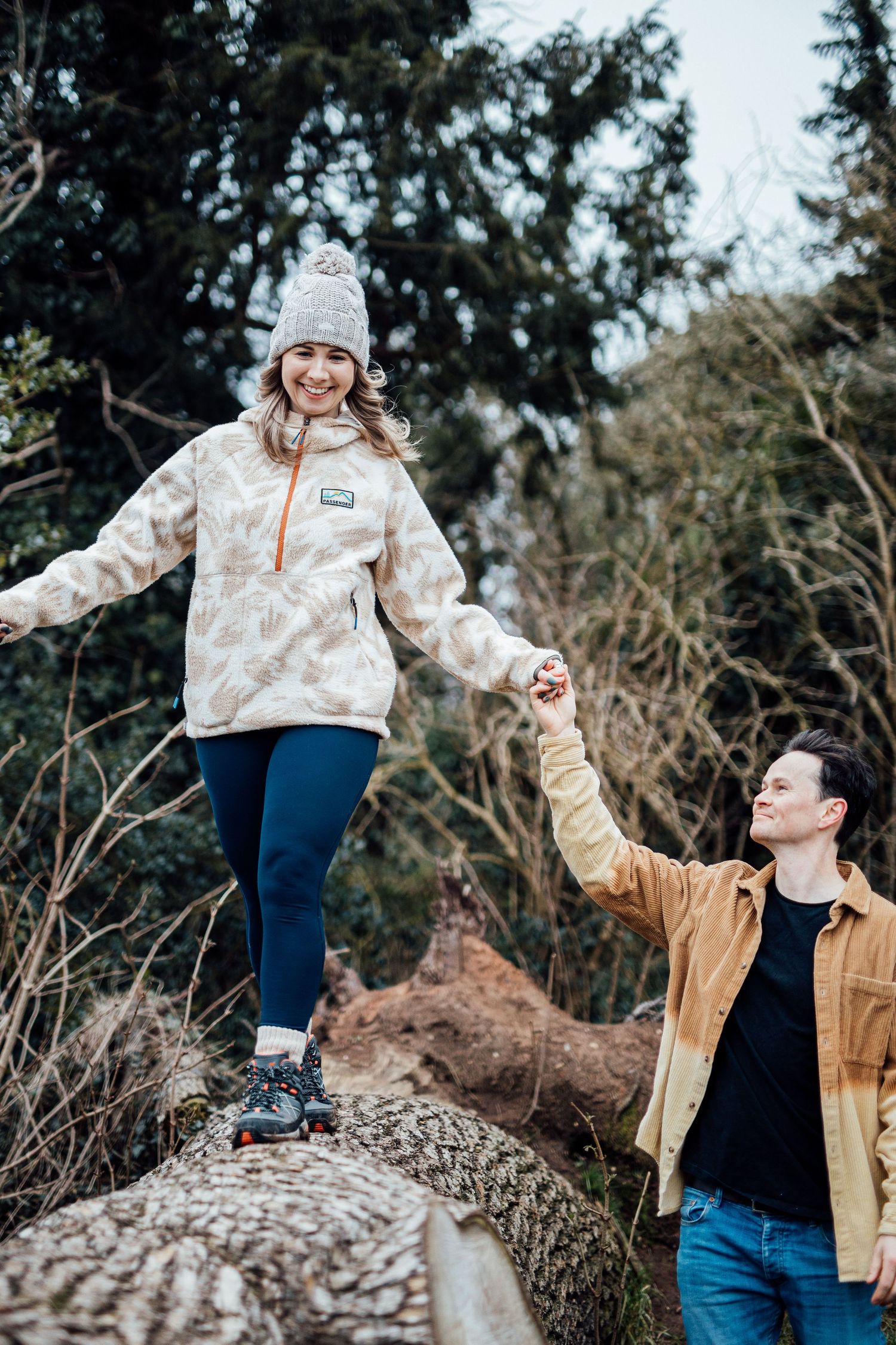 Playful couple balancing on a large rock during an outdoor photo session.