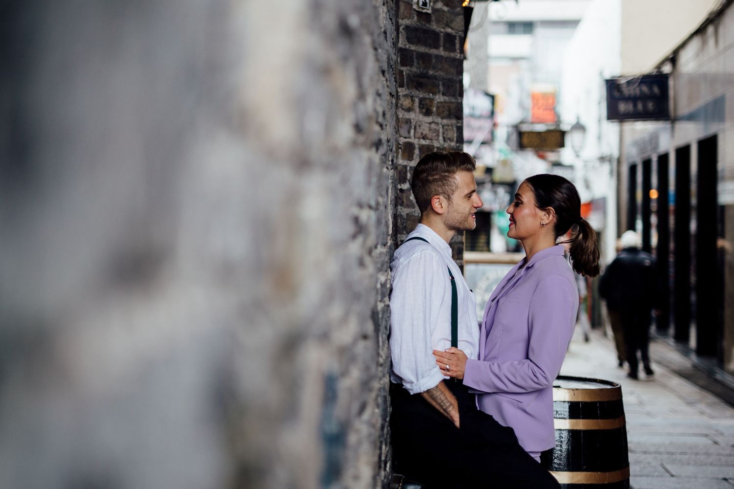 A couple shares an intimate moment against a brick wall in an urban alley.