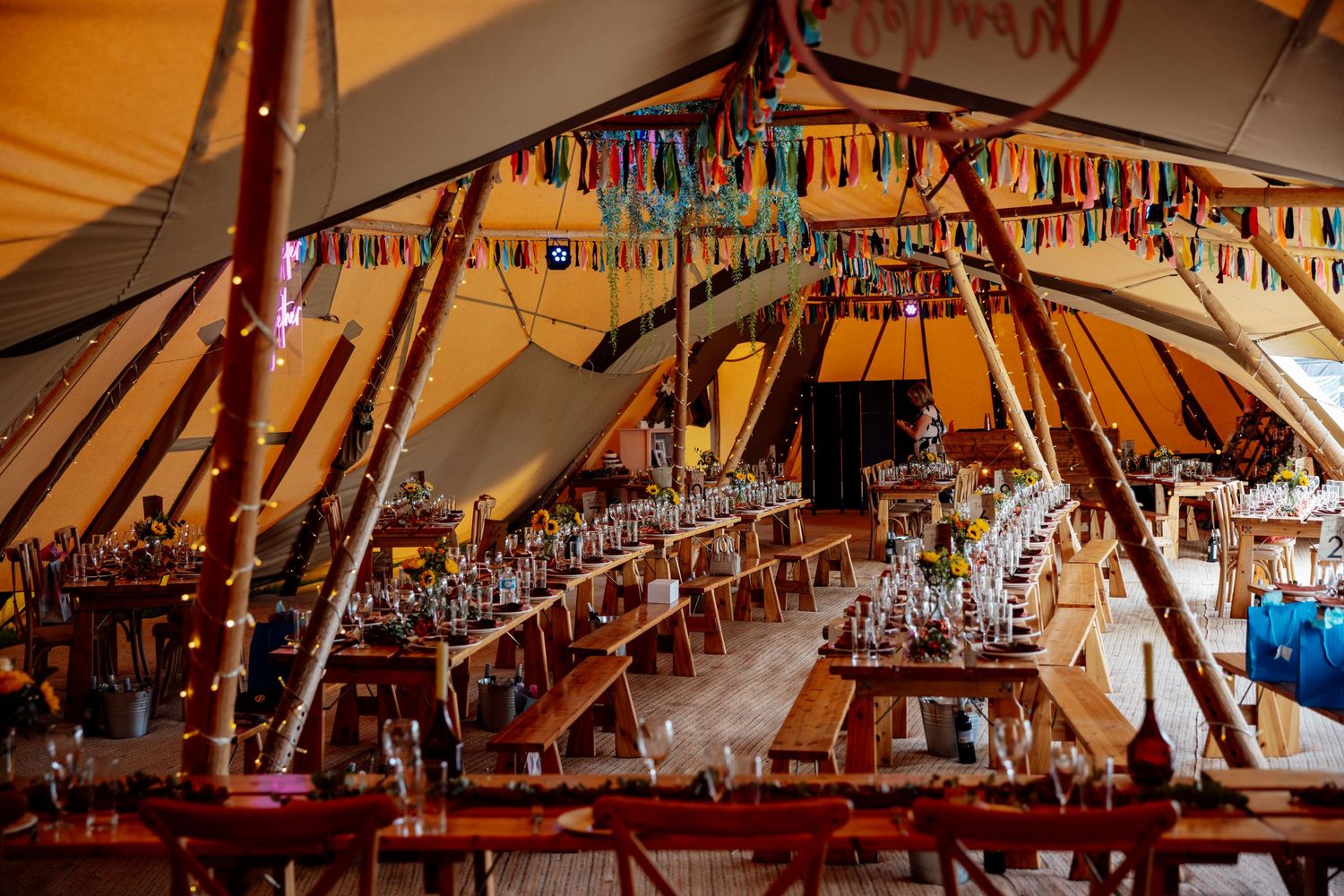 Interior of a decorated tipi tent with long tables set for a wedding reception.