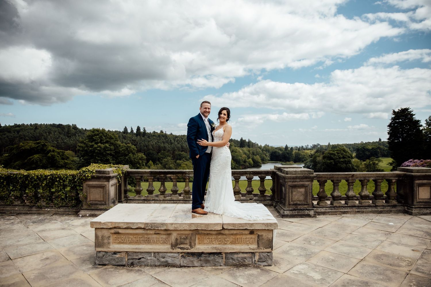 Panoramic view of a wedding celebration on a grand stone terrace under cloudy skies.