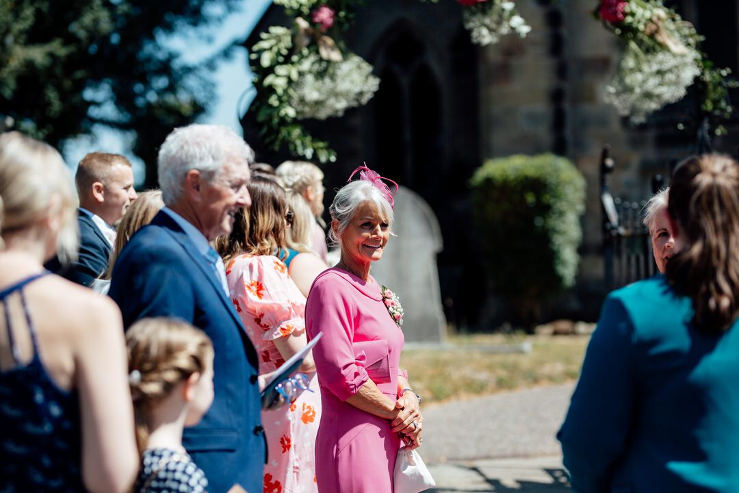 Wedding guests gathered outside a church on a sunny afternoon.