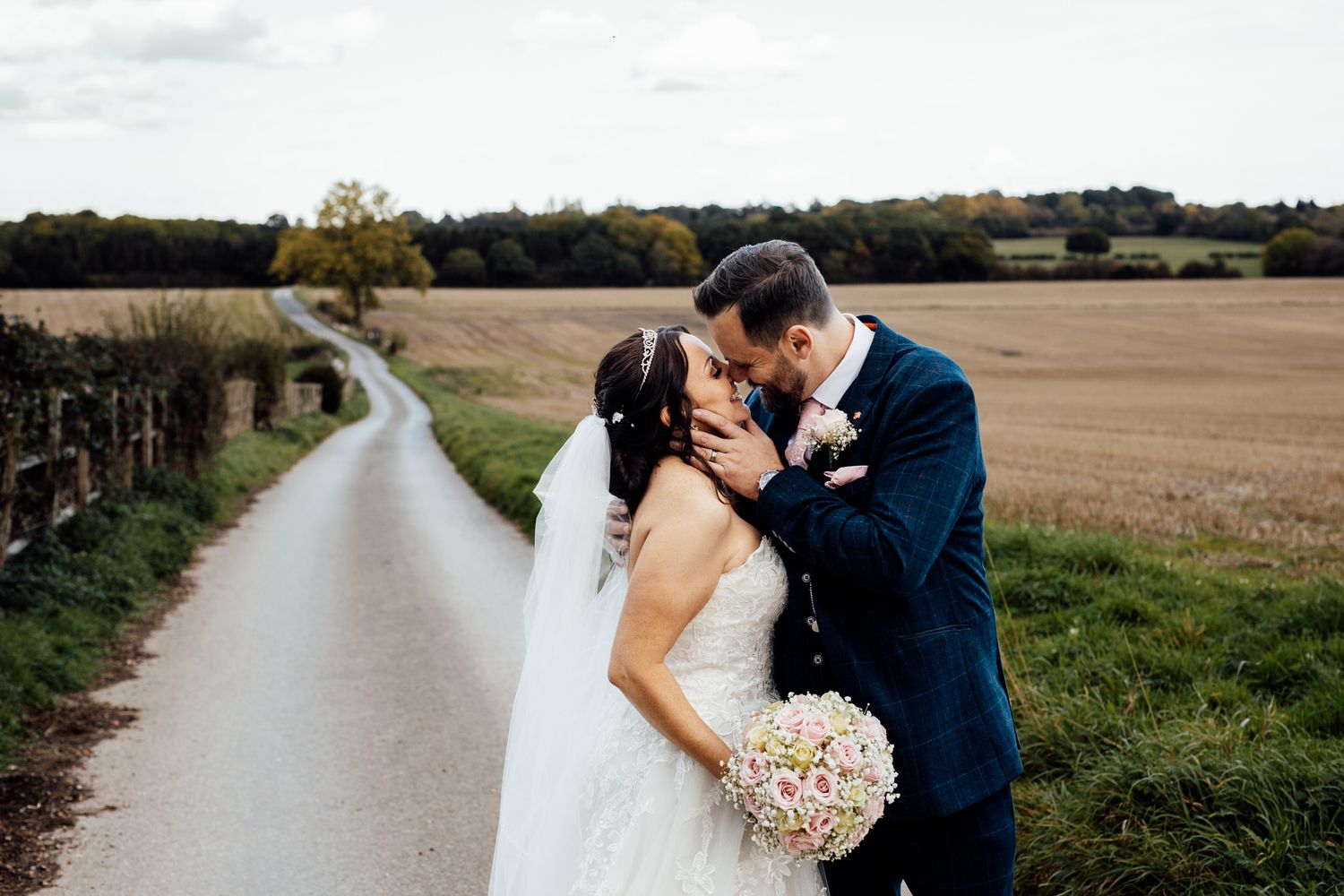 A romantic countryside wedding photo with the couple kissing on a winding rural road.