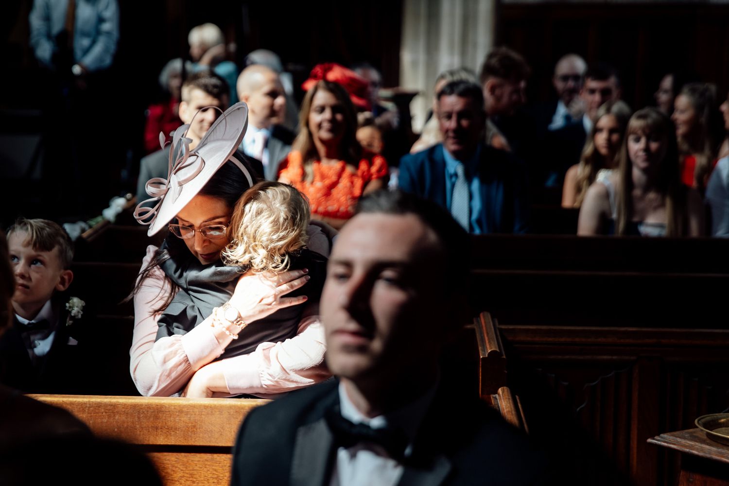 Wedding guests seated in dark wooden church pews during ceremony.