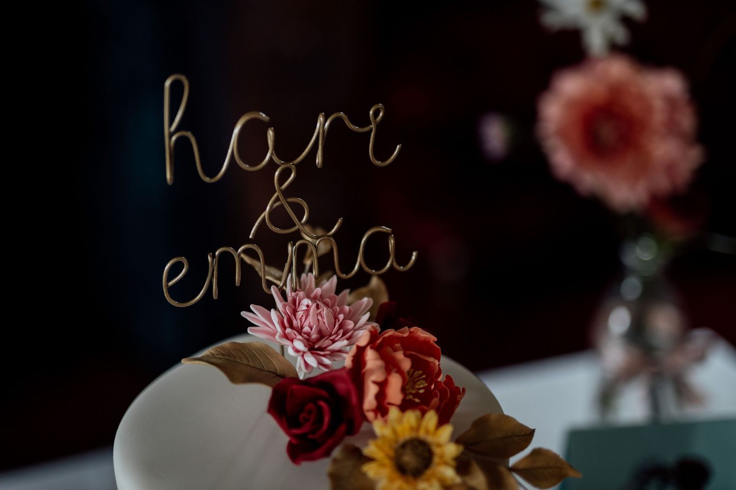 Wedding cake topper with cursive text surrounded by delicate floral decorations.