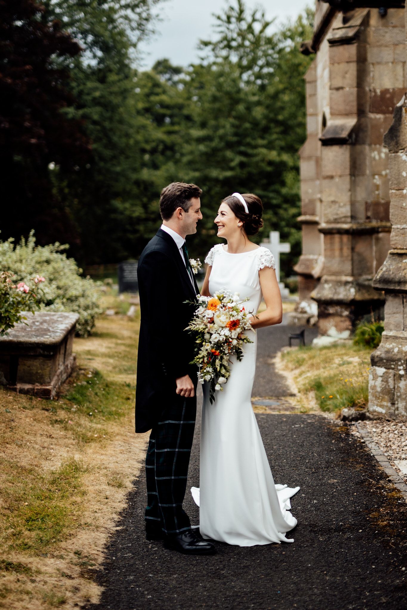 Couple walking along a stone church path surrounded by summer greenery.